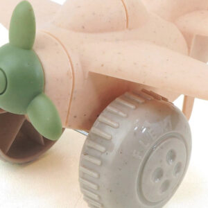 Avión de juguete en color rosa suave, con hélices verdes y ruedas en un tono marrón claro.